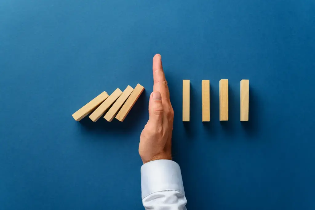 Hand stopping a line of falling dominoes